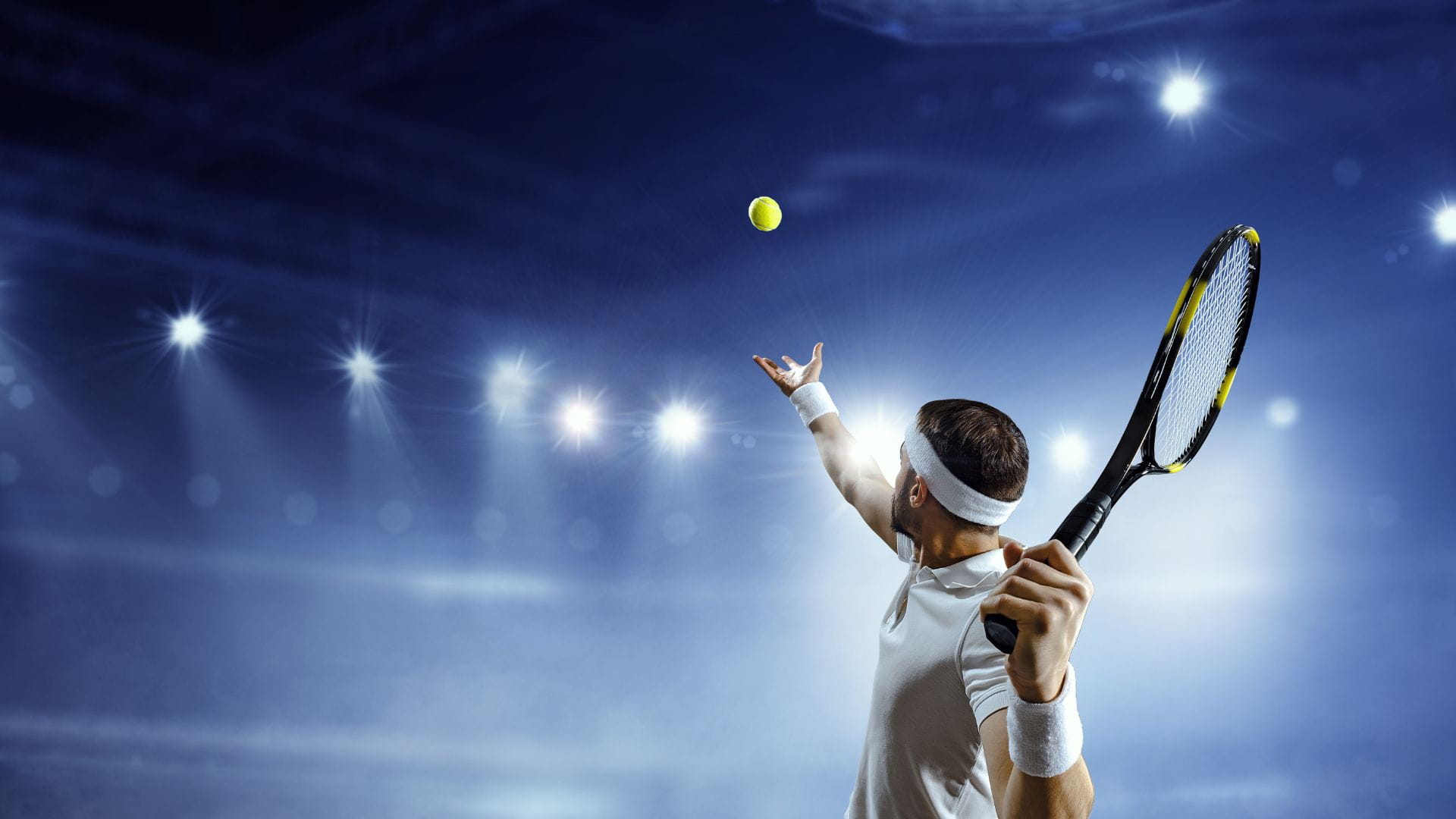 Professional tennis player serving under stadium lights during a major international tournament reached by private charter.